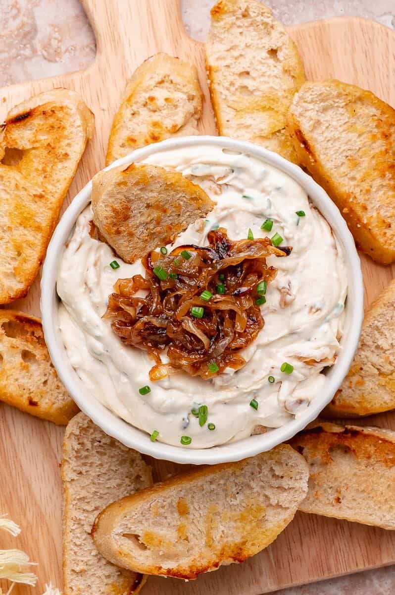 Caramelized onion dip in a bowl surrounded with crostini and garnished with more caramelized onions.