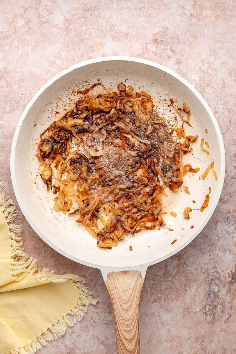 Onion slices are cooking in a skillet until they are caramelized with seasonings.