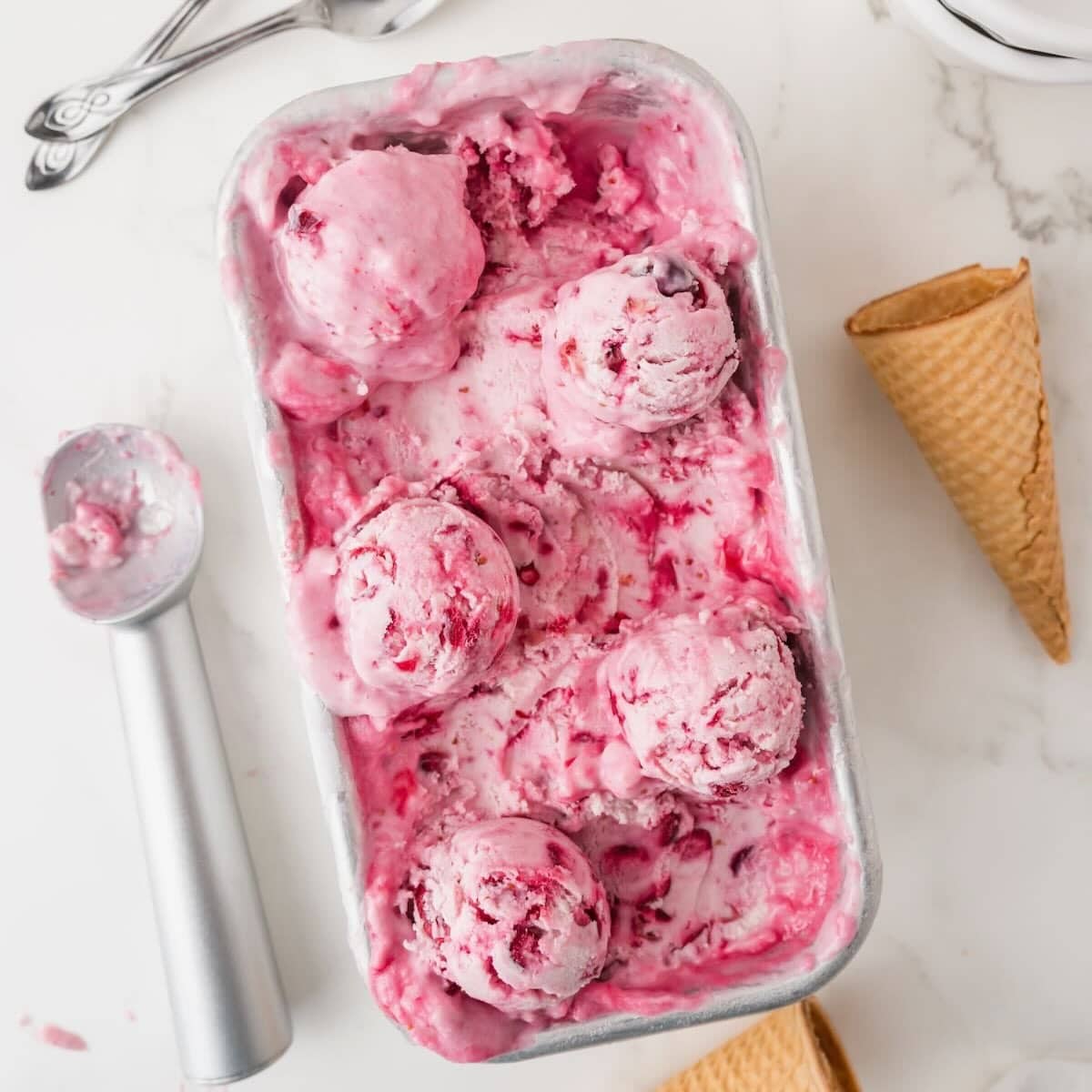 A loaf pan with frozen cranberry ice cream with scoops of the ice cream on top.