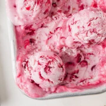 Cranberry ice cream in a metal loaf pan, with scoops of the ice cream on top.