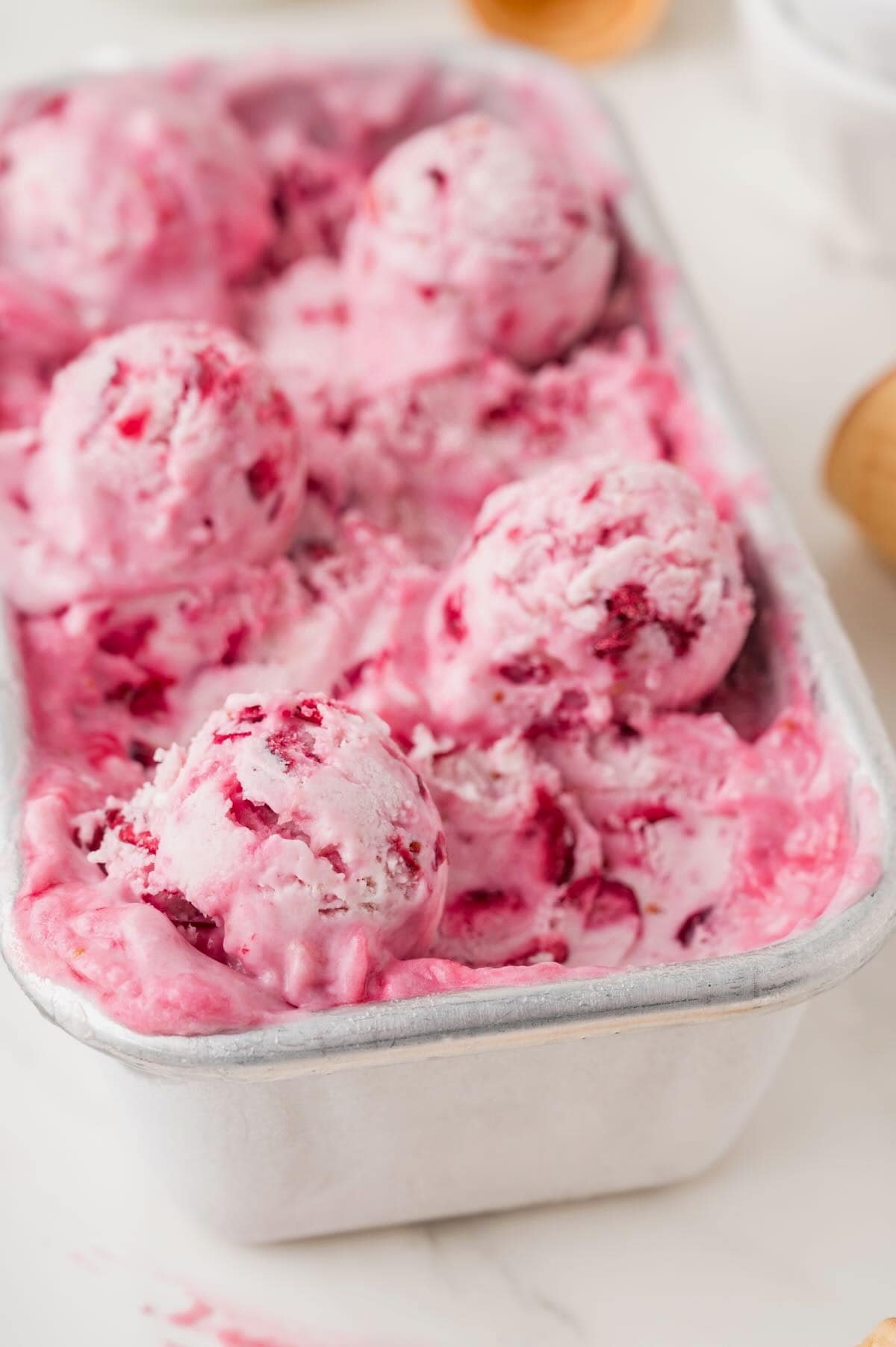 A metal loaf pan full of homemade cranberry ice cream topped with scoops of ice cream.