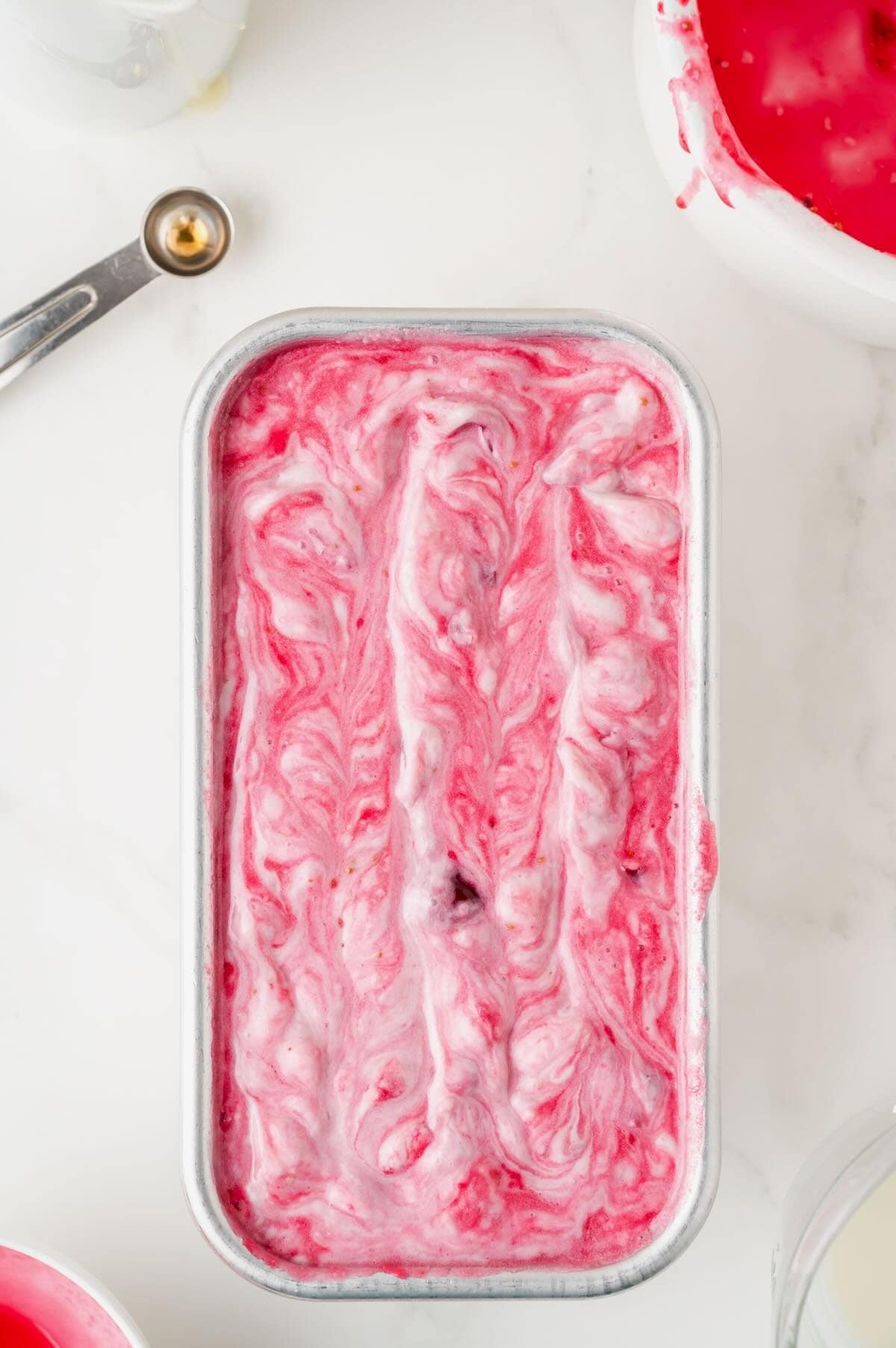 A loaf pan full of cranberry ice cream is ready to freeze.