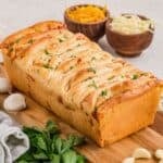 A golden brown loaf of garlic cheese pull-apart bread on a cutting board.