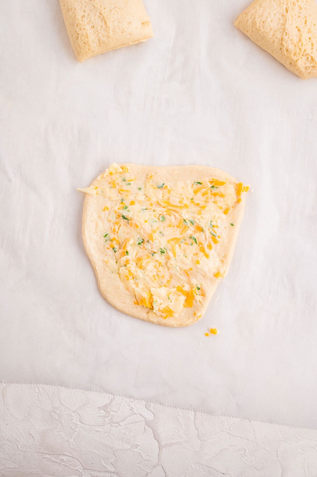 A rolled out piece of bread dough with a cheese, garlic butter mixture spread on it.