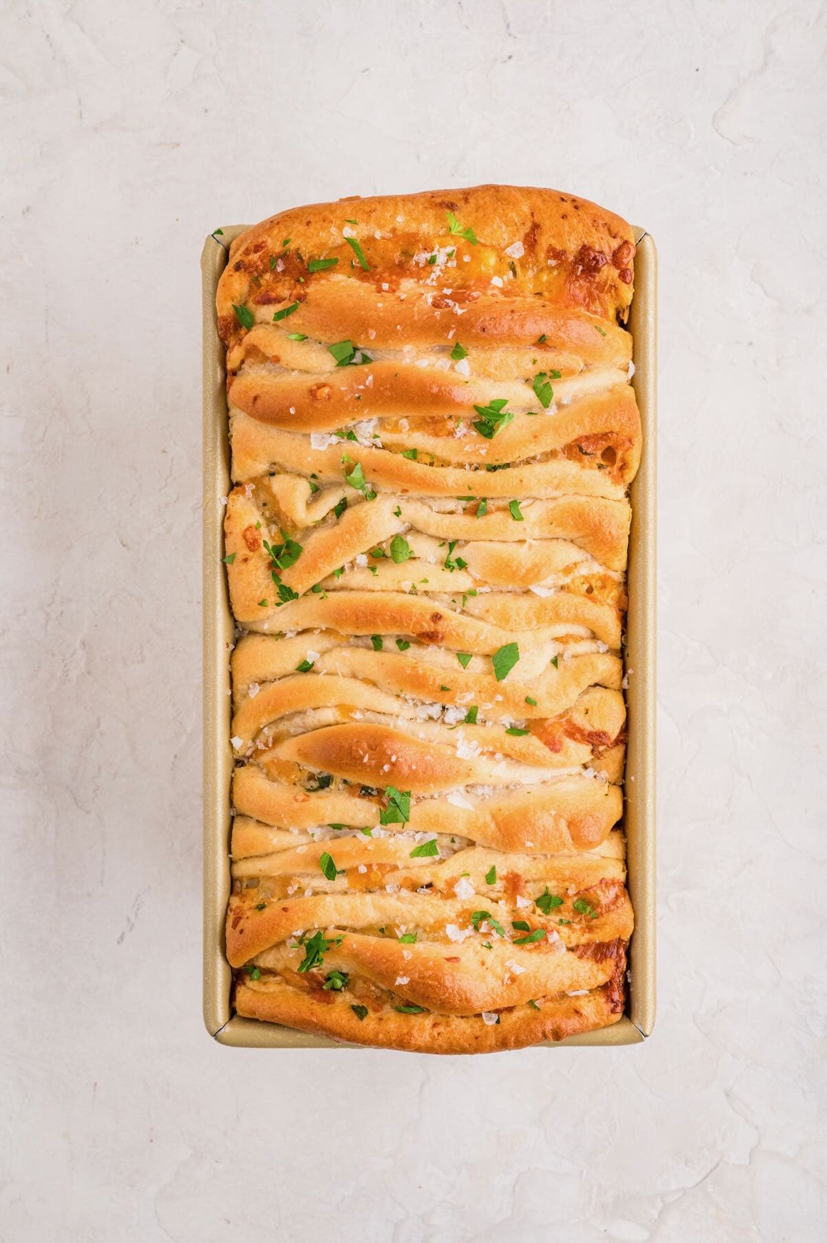 A loaf of baked garlic cheese pull-apart bread garnished with melted butter, salt, and parsley.
