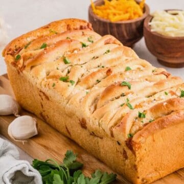 A golden brown loaf of garlic cheese pull apart bread on a cutting board.