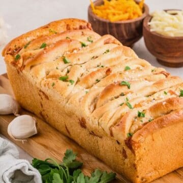 A golden brown loaf of garlic cheese pull apart bread on a cutting board.