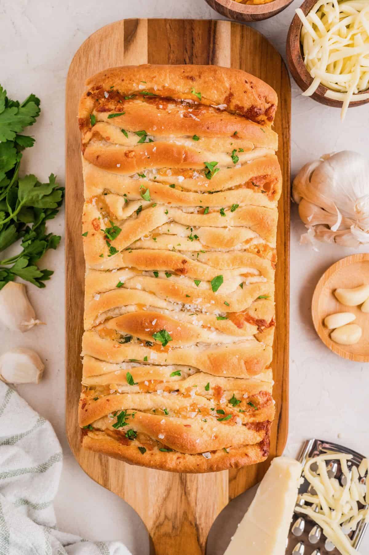 A loaf of garlic cheese pull apart bread that has been baked on a cutting board.