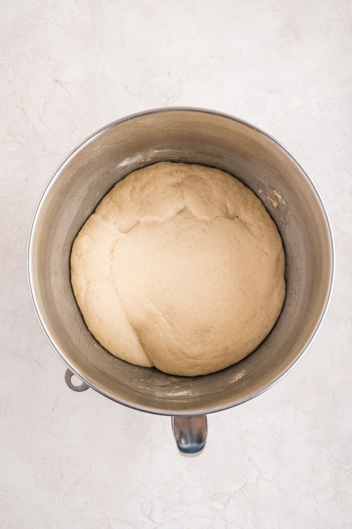 A ball of dough in a metal mixing bowl that has risen.