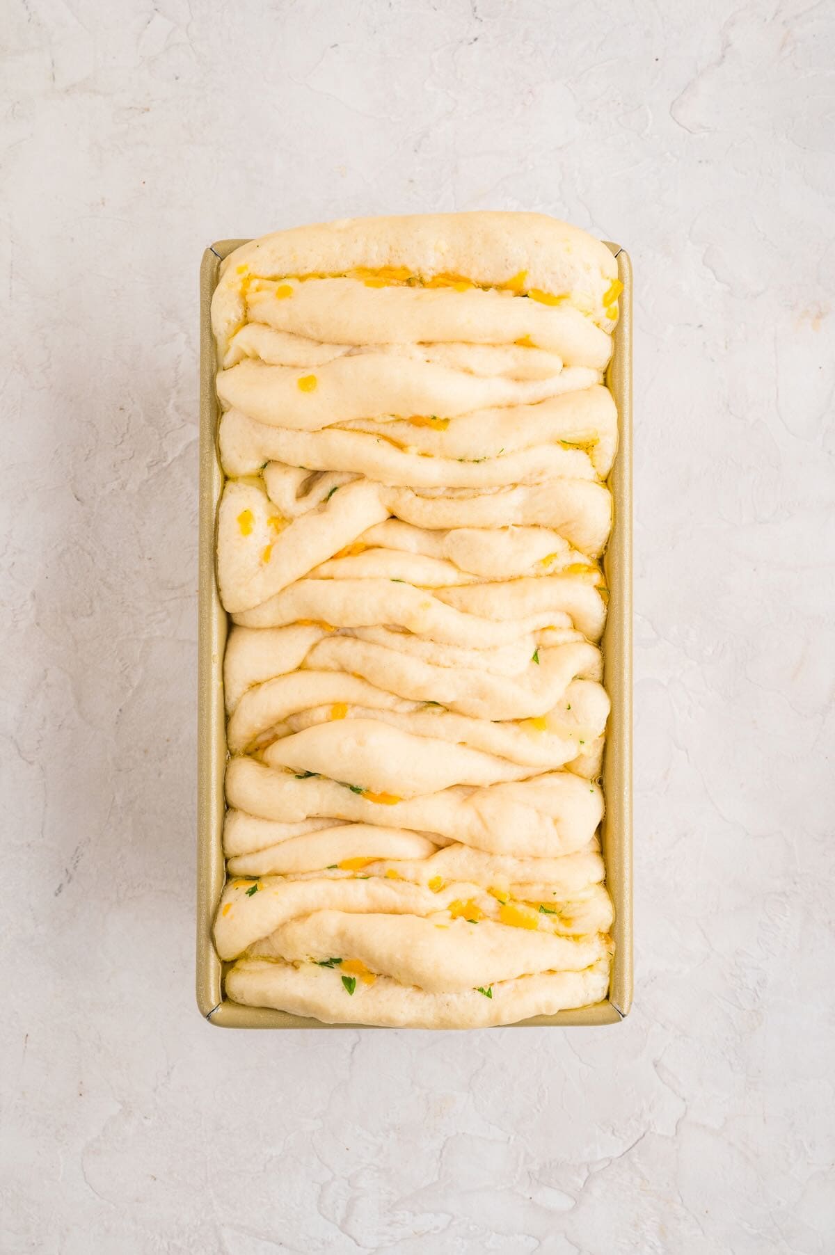 A loaf pan full of pieces of bread dough that have a cheese and butter mixture spread on them.