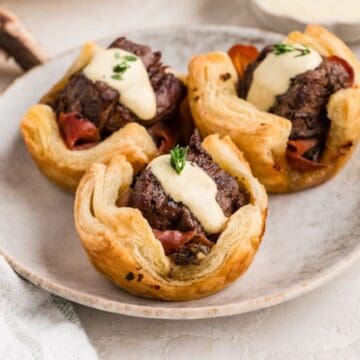 Three Beef Wellington Bites on a plate topped with horseradish sauce and fresh thyme.