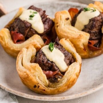 A plate with three mini Beef Wellington Bites topped with horseradish sauce and fresh thyme.