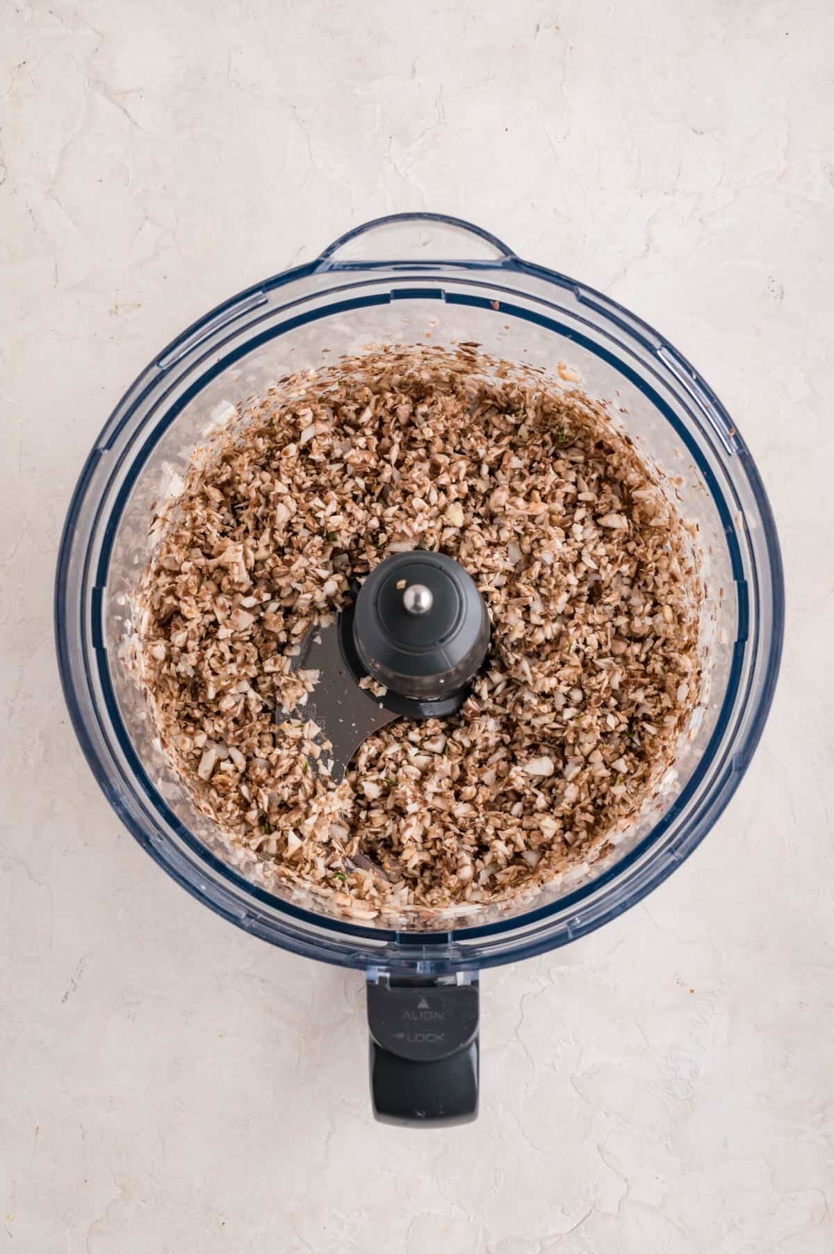 Mushrooms, onion garlic, and thyme chopped up in the bowl of a food processor.