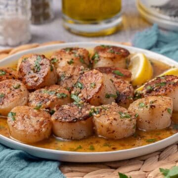 A serving plate full of pan seared scallops cooked in a cast iron skillet and topped with garlic butter.