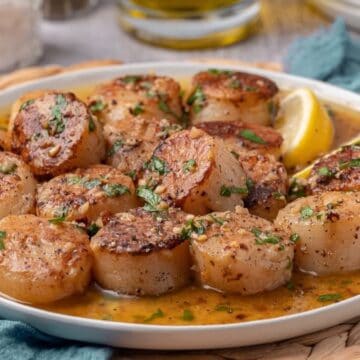 A serving platter of garlic butter, cast-iron-seared scallops, garnished with chopped parsley.
