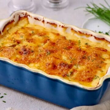 Baked cheesy scalloped potatoes in a blue baking dish with a bundle of chives next to it.