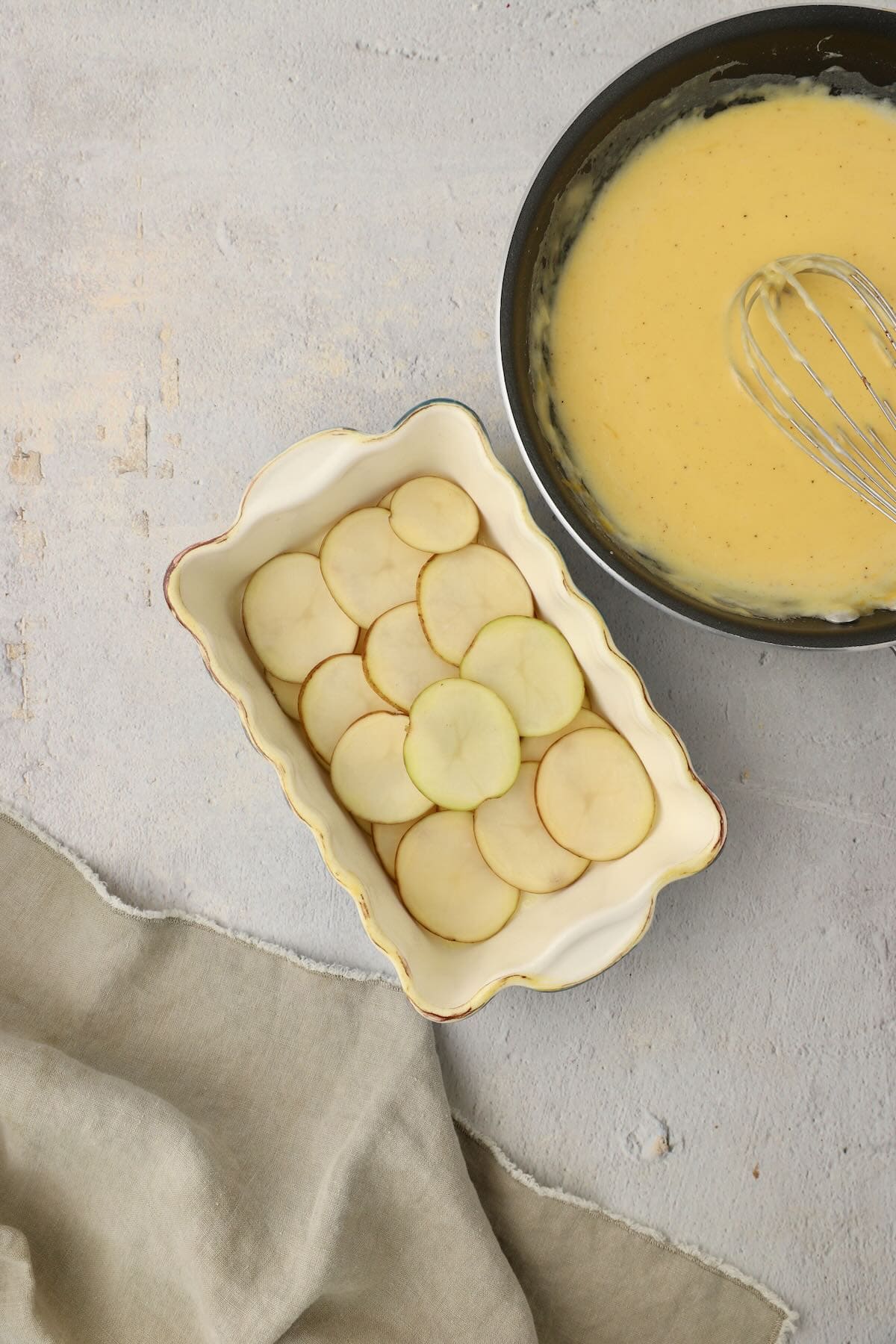 Cheese sauce and a layer of sliced potatoes in a baking dish.