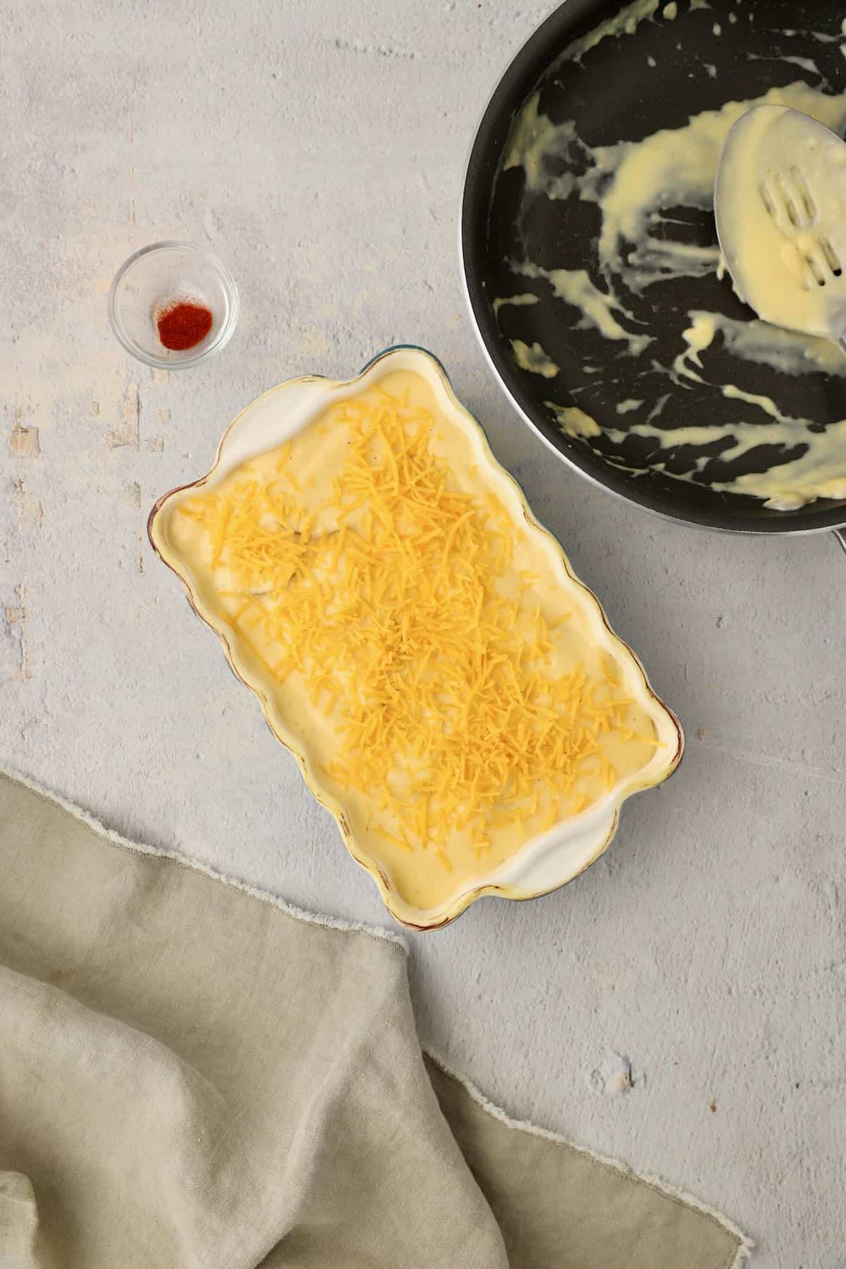 Cheese scalloped potatoes in a baking dish topped with shredded cheddar and parmesan cheeses.