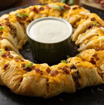 A baked Chicken Bacon Ranch Crescent Roll Ring with a bowl of dipping sauce in the middle.
