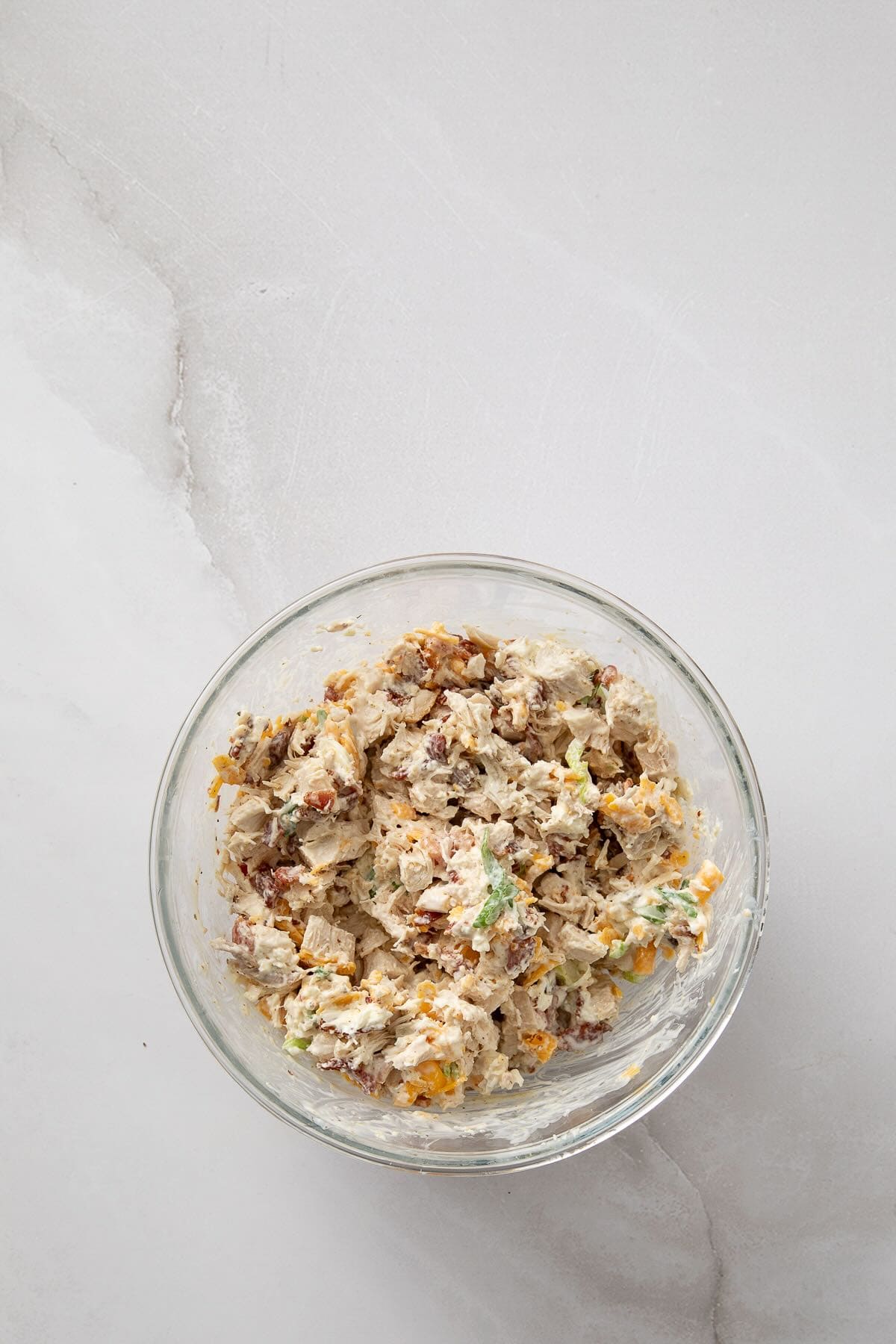 A bowl of cooked chicken, bacon, ranch dressing, and cheese.