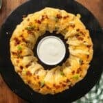 Chicken Bacon Ranch Crescent Ring on a black platter with a bowl of dip in the middle.