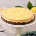 A lemon cheesecake topped with lemon curd on a white cake plate.