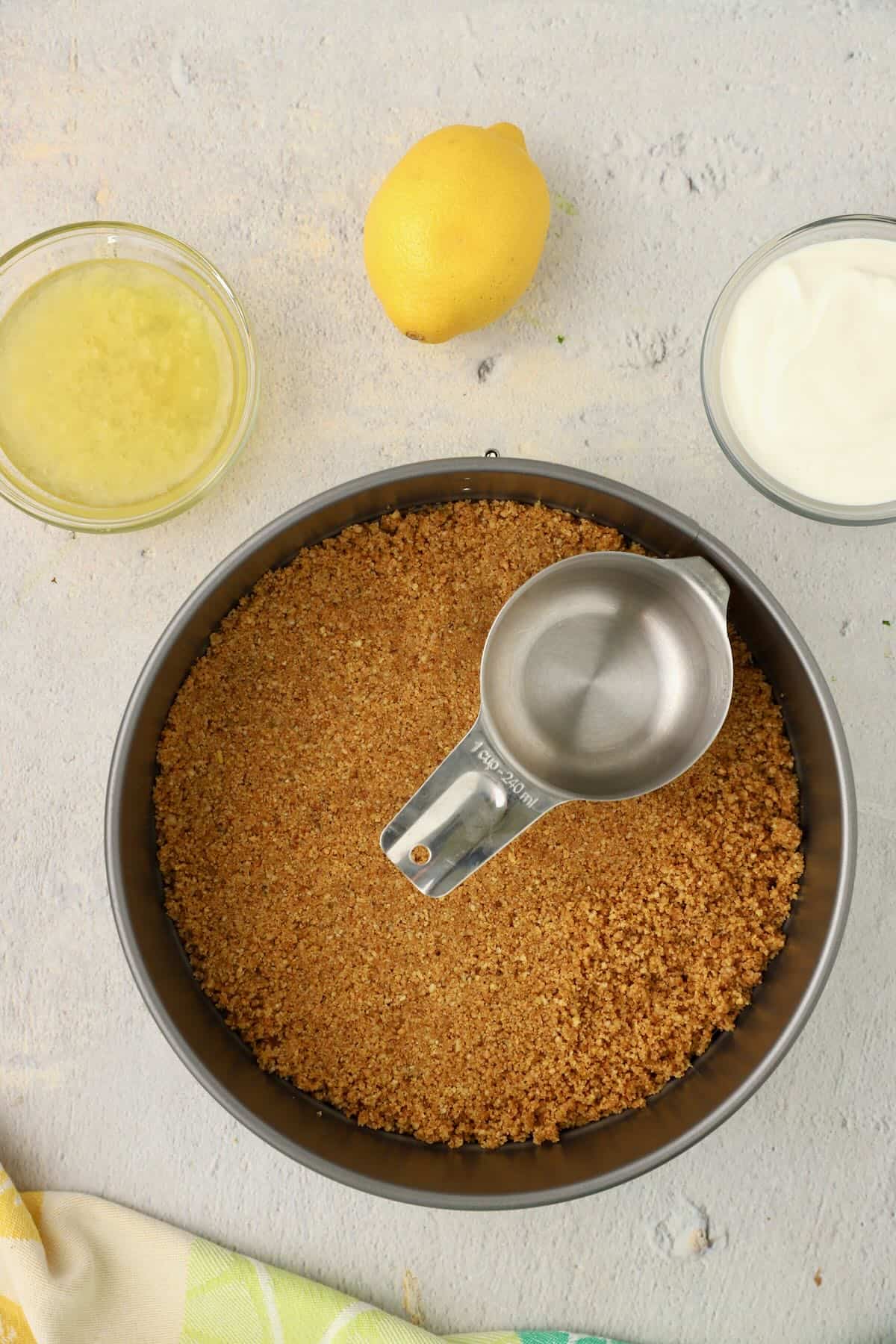 A springform pan with a graham cracker crust being added and smoothed out.