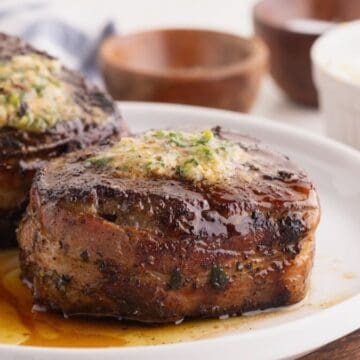 Two bacon wrapped filet mignons topped with melted cowboy butter on a plate.