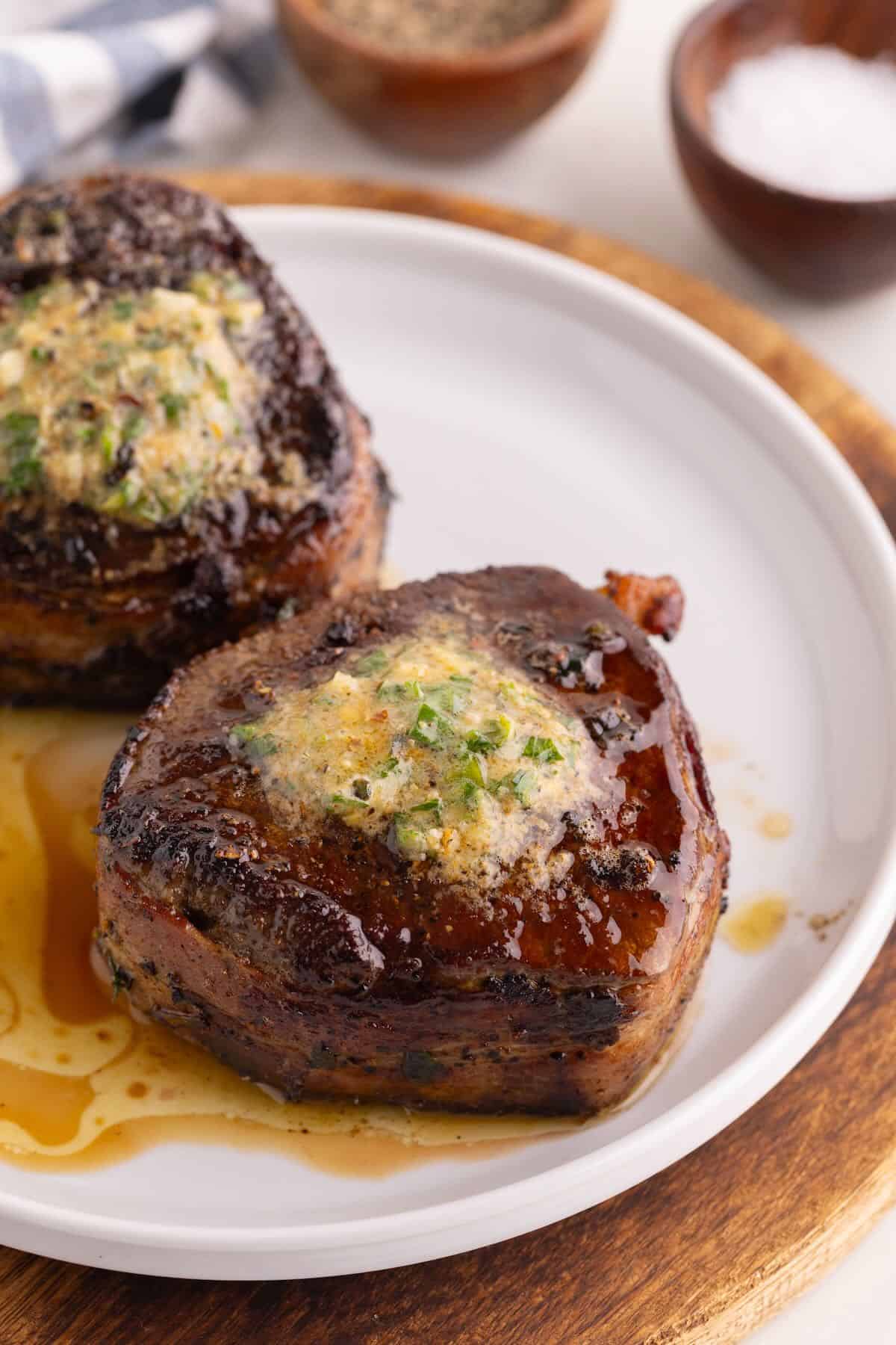 Two bacon-wrapped filet mignons cooked in a cast iron skillet topped with cowboy butter on a plate.