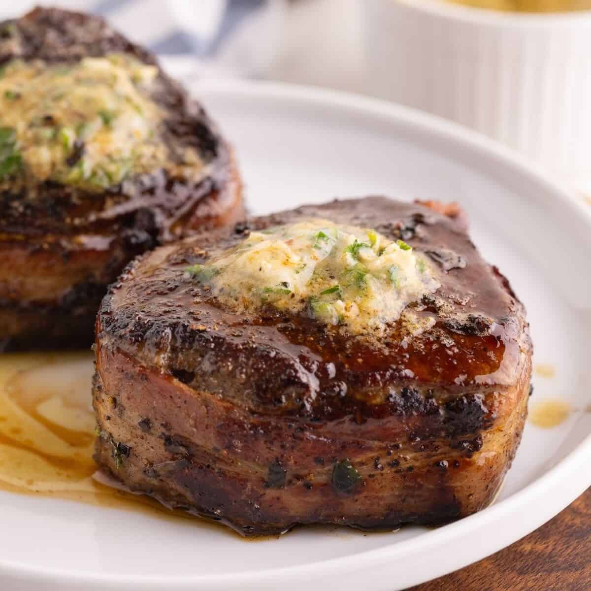 Two bacon wrapped filet mignons topped with melted cowboy butter on a plate.