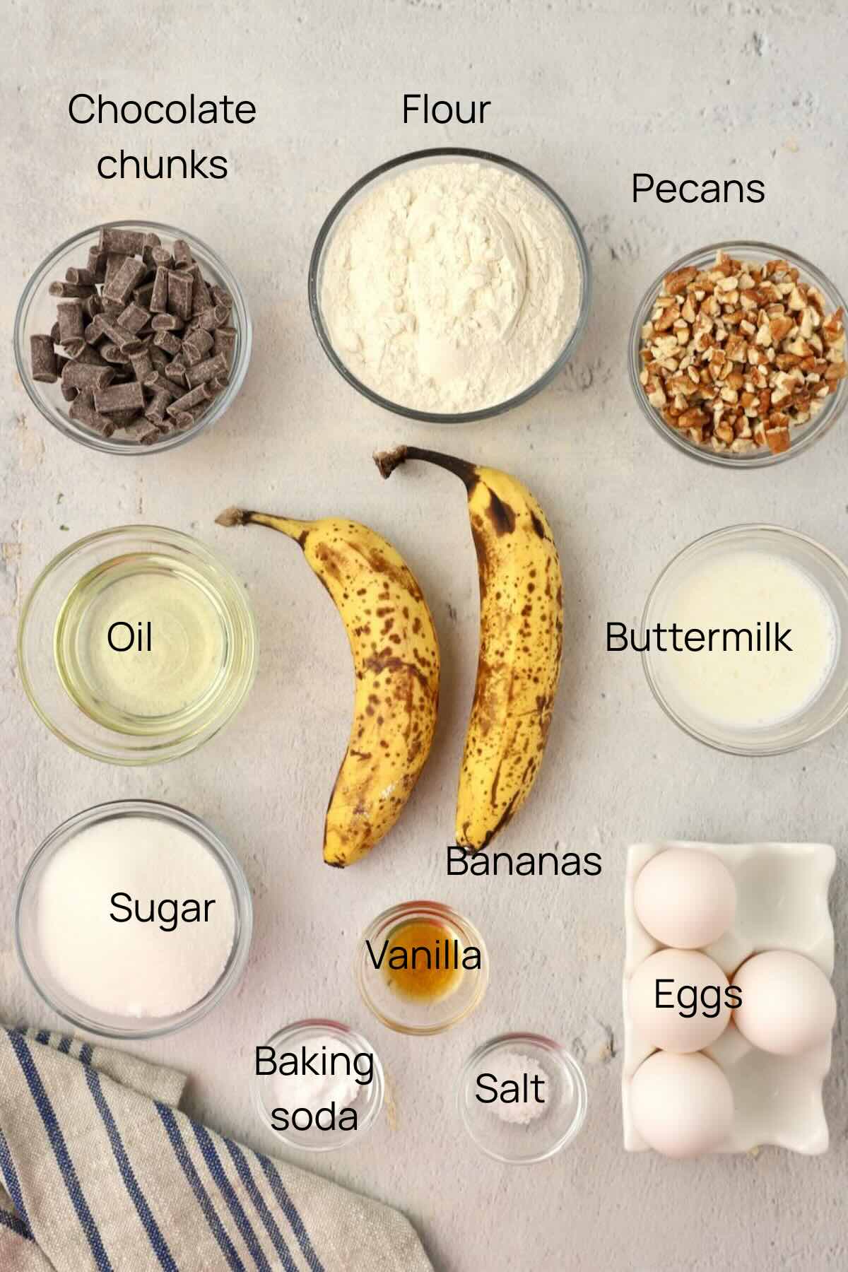 Ingredients to make chocolate chunk banana bread include flour, chocolate chunks, eggs, sugar, and pecans.