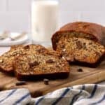 A loaf of chocolate chunk banana bread with slices cut on a cutting board.