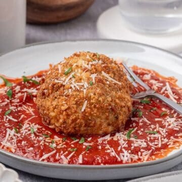 A fried burrata ball in a bed of marinara sauce topped with a sprinkle of grated parmesan cheese.