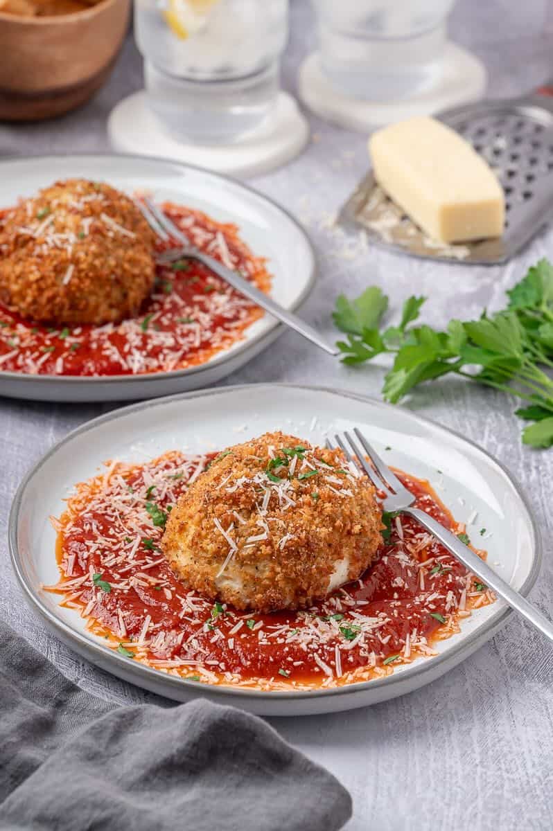 Two plates with fried burrata balls on top of marinara sauce with topped with a sprinkle of parmesan cheese.