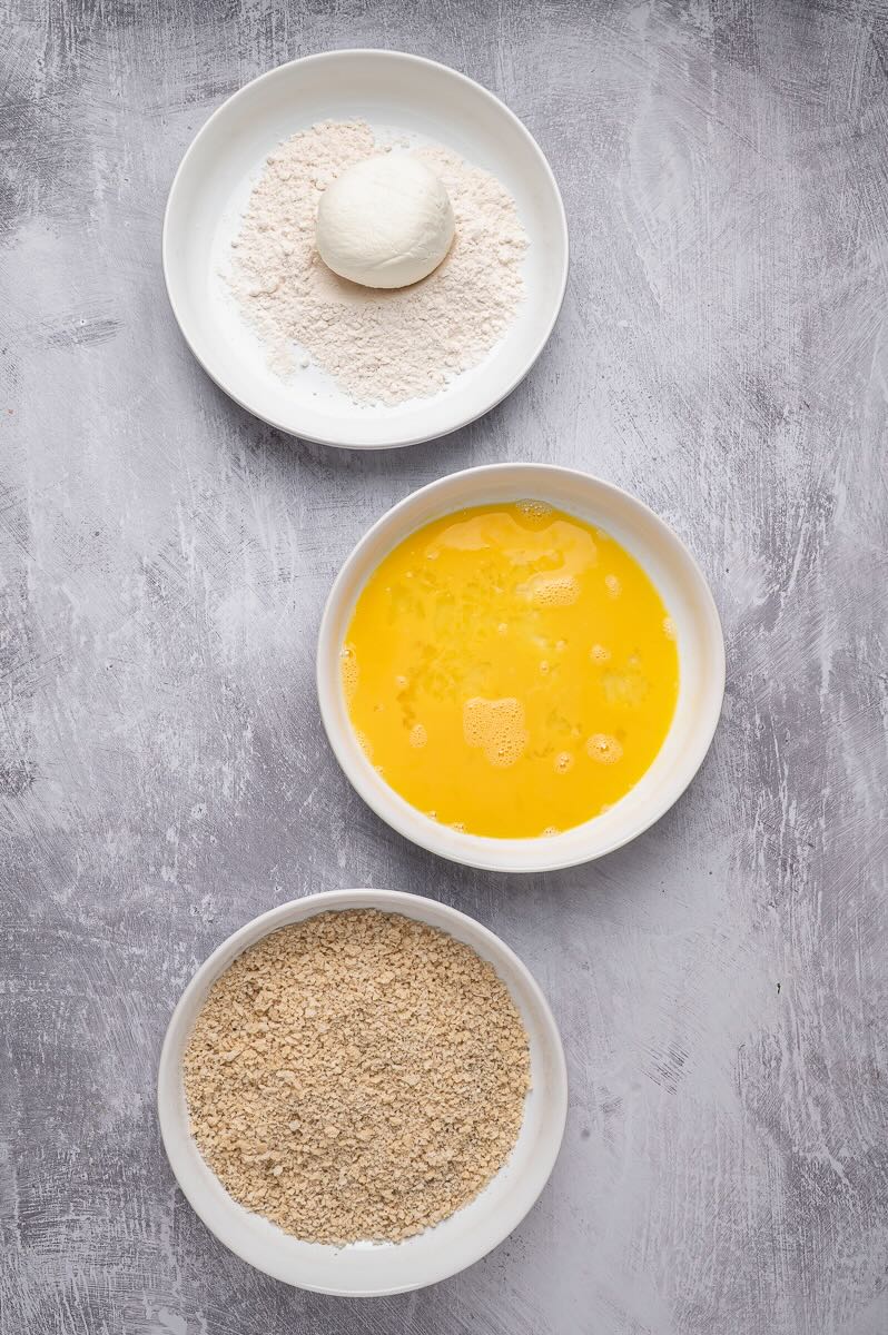 Three bowls, flour, egg, and panko with burrata in the flour one.