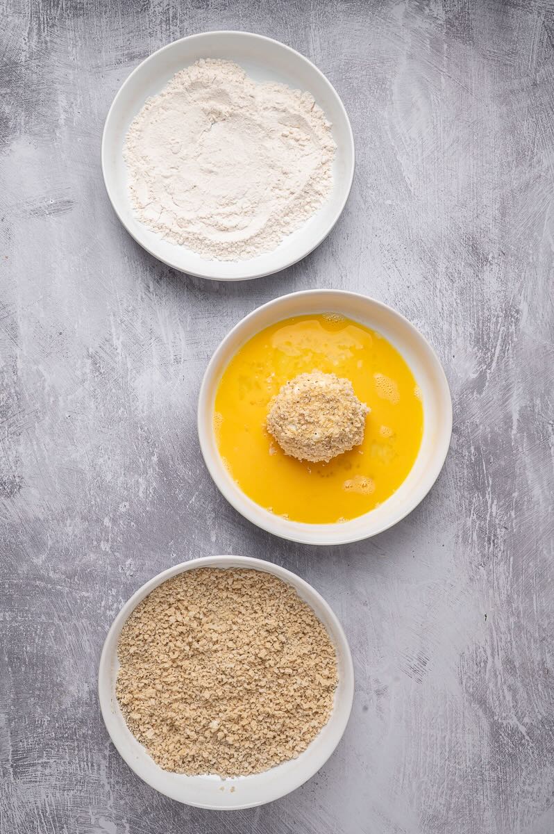 Three bowls, one with flour, one with egg, and the last with panko, and burrata in the egg mixture.