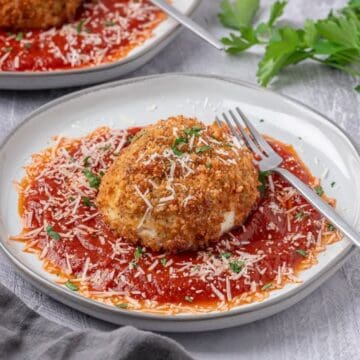 A fried burrata ball in a bed of marinara sauce topped with a sprinkle of grated parmesan cheese.