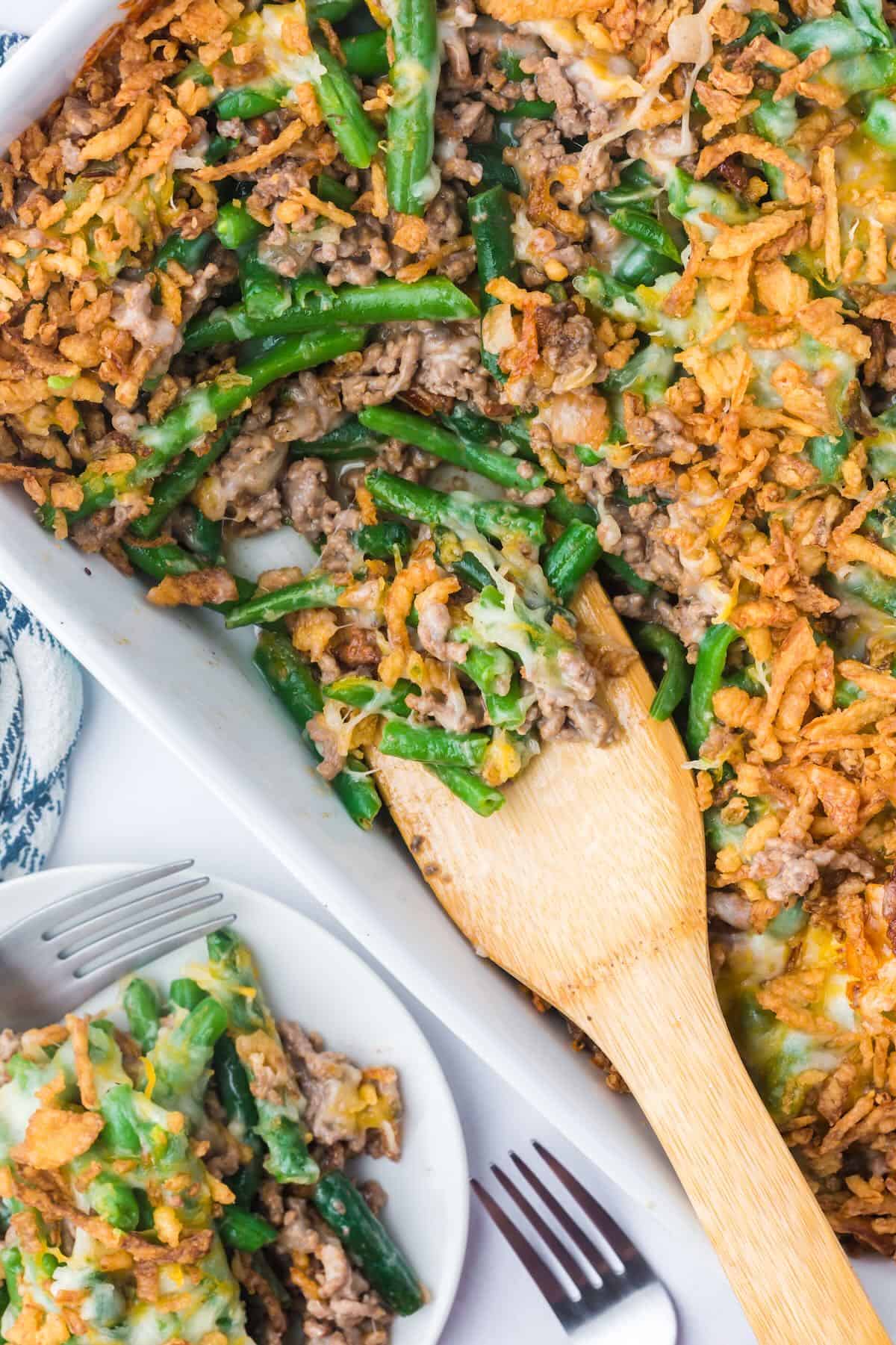 A serving of hamburger green bean casserole is on a wooden spoon. 