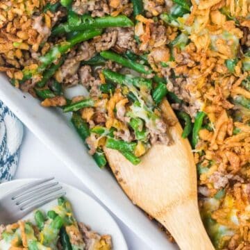 Baked hamburger green bean casserole with a wooden spoon.