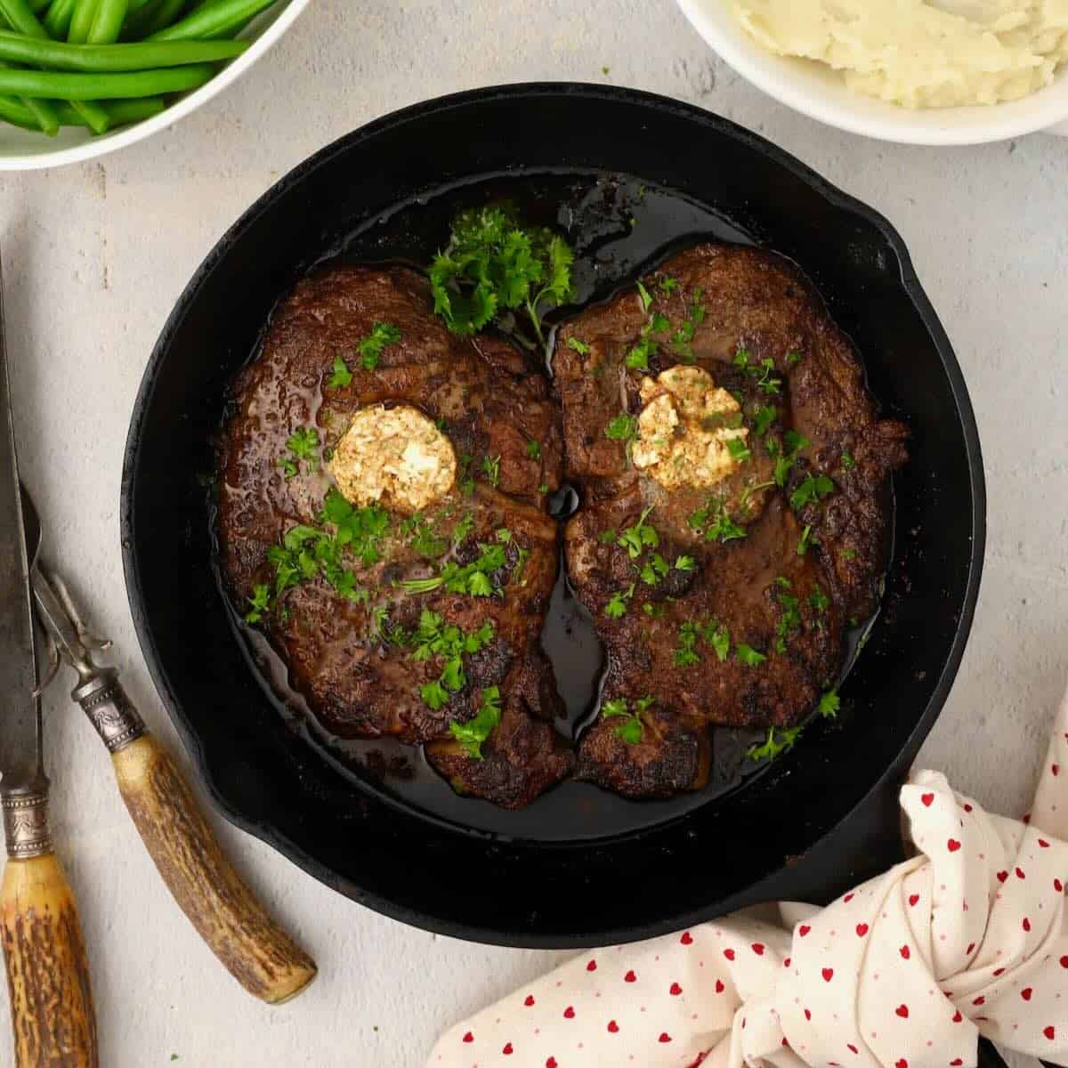 Pan seared ribeyes in a cast iron skillet placed side by side to make a heart.