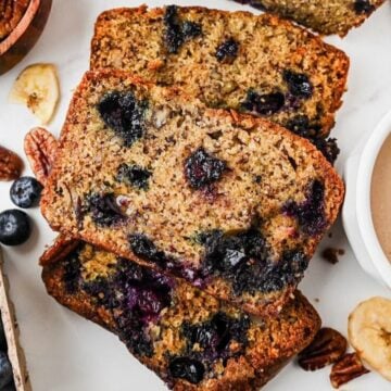 Slices of blueberry banana nut bread next to a carton of blueberries and a bowl of pecans.