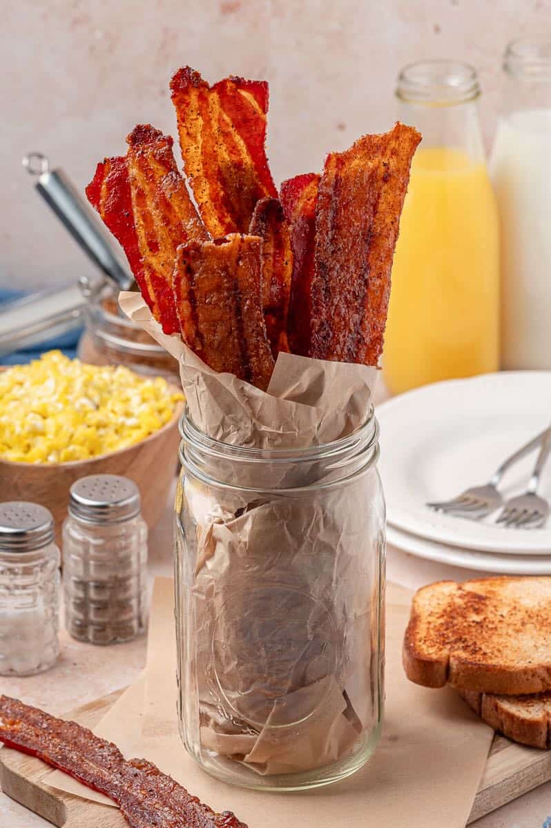 A jar lined with parchment paper full of brown sugar sweet and spicy bacon.