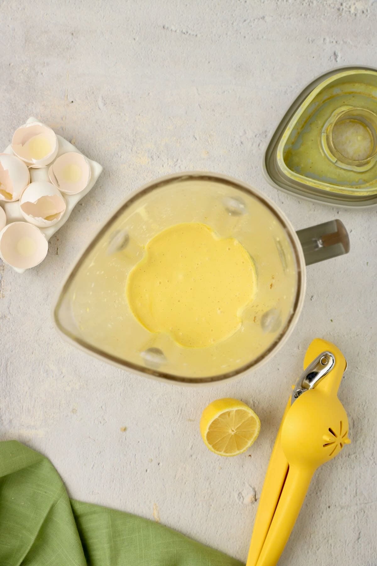 Looking down in a blender jar are egg yolks, lemon juice and seasonings mixed together.