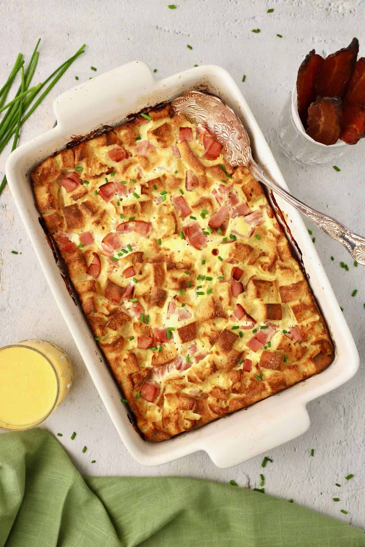 Baked eggs benedict casserole garnished with chopped chives in a baking dish with a spoon.