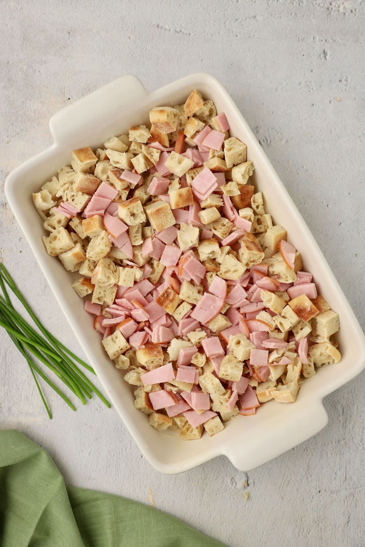 Chopped english muffins and canadian bacon mixed in a large white baking dish.