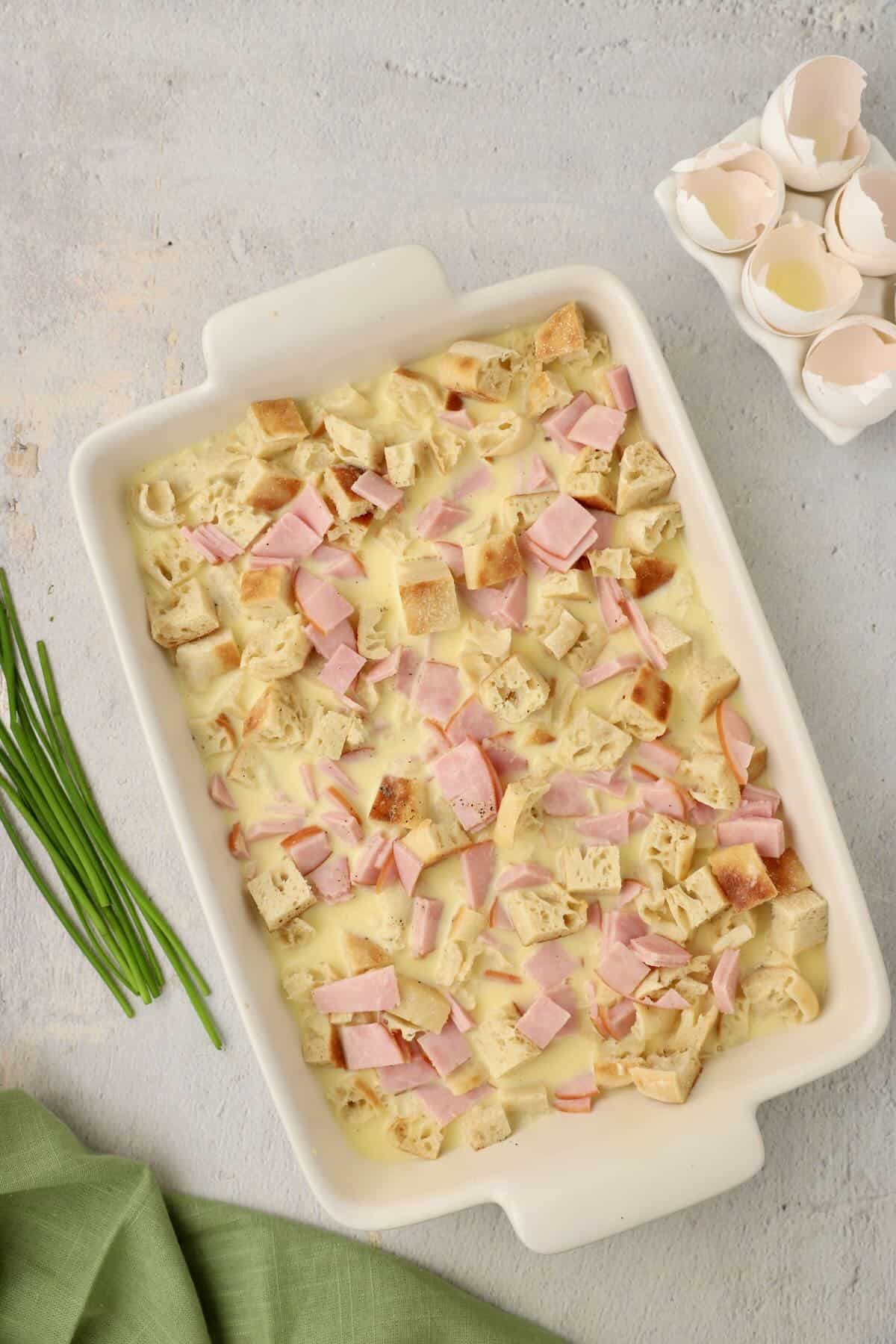 Unbaked eggs benedict casserole with custard in a baking dish ready to refrigerate.