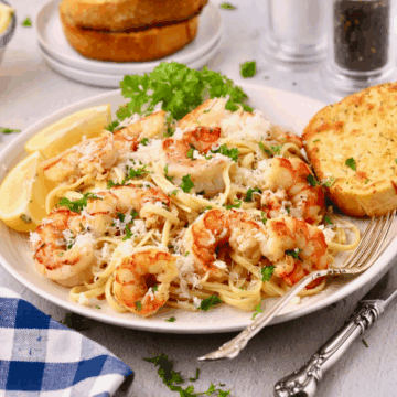 A plate full of garlic butter noodles with shrimp with a piece of garlic toast on the side.