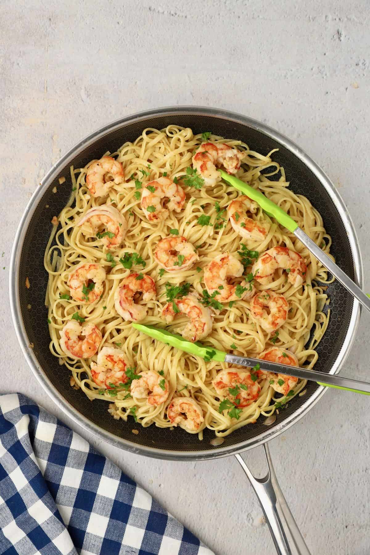 A skillet full of garlic butter noodles with tongs, ready to serve.