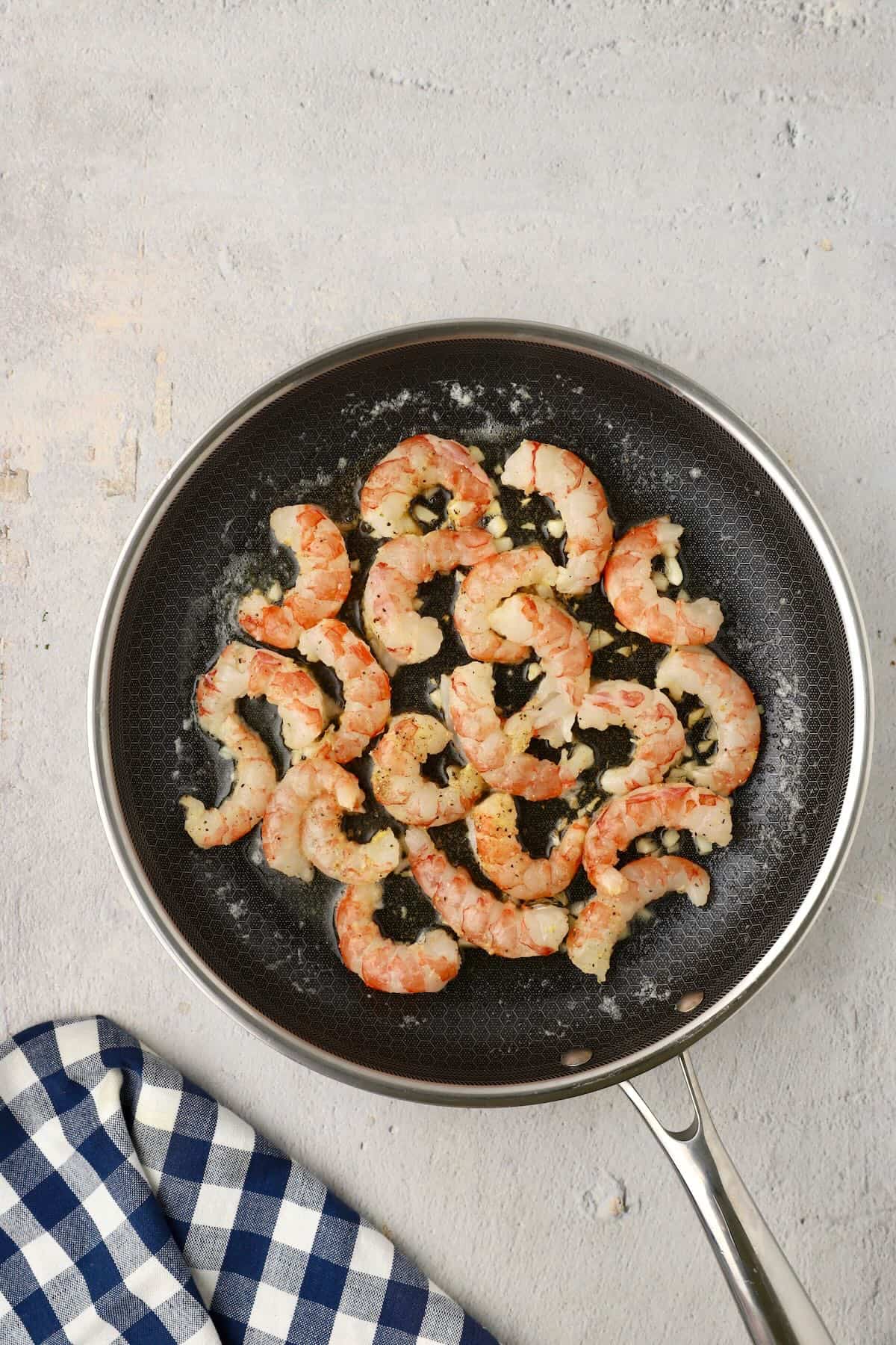 Shrimp cooking in butter and olive oil in a skillet.