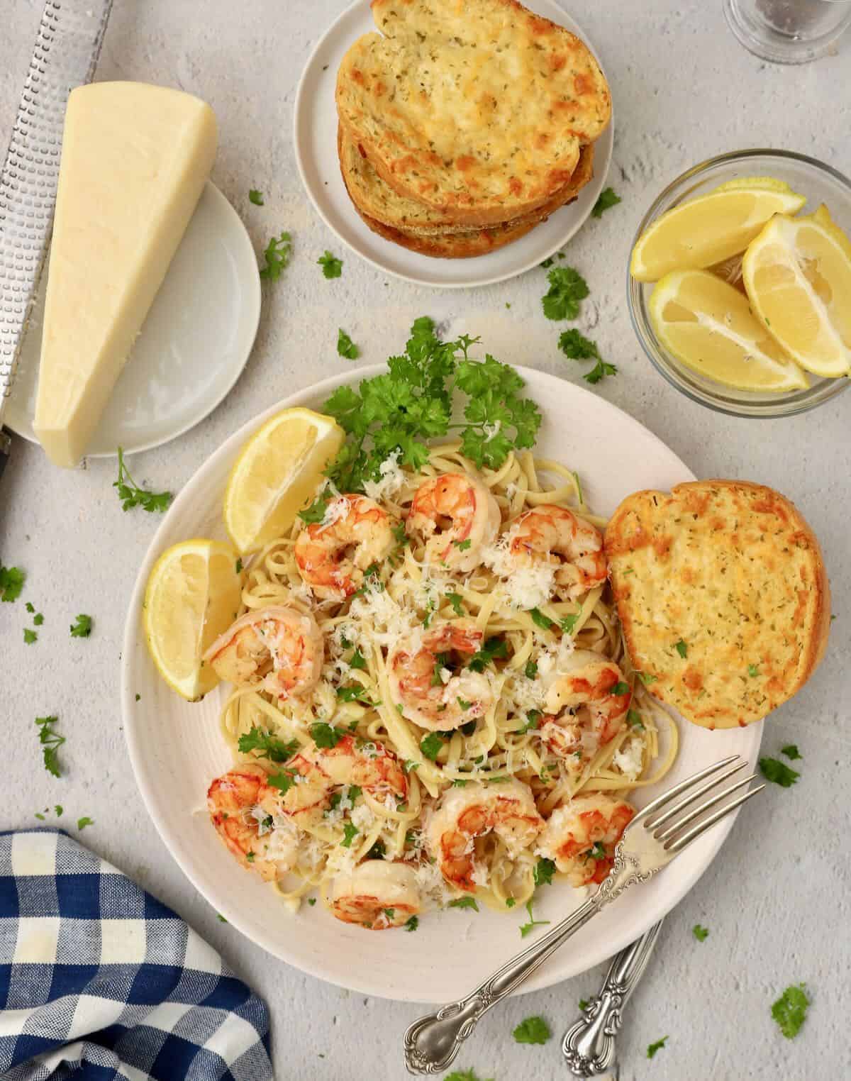 A plate full of garlic butter noodles with shrimp topped with parsley and Parmesan cheese served with garlic toast.